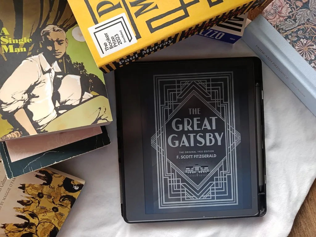 A photo of The Great Gatsby by F. Scott Fitzgerald open on a Kindle Scribe with some books in the background for decor