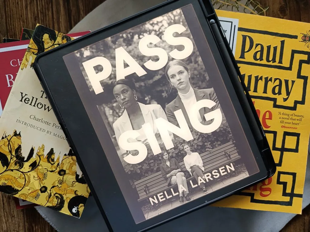 A photo of Passing by Nella Larsen open on Kindle scribe against a background of books for decor