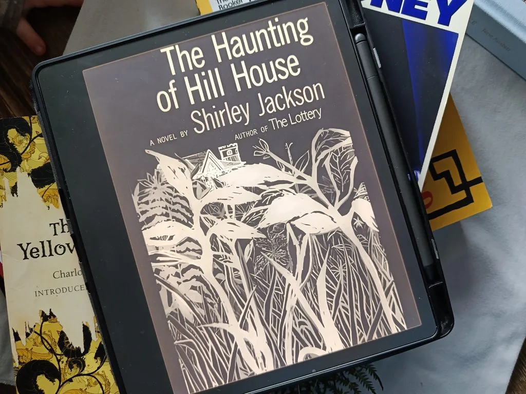 A photo of The Haunting of Hill House open on Kindle Scribe against a background of books