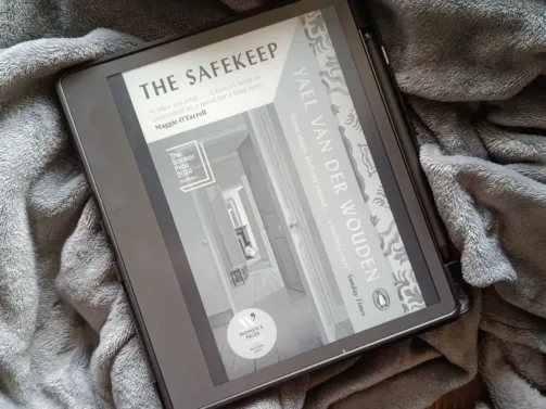 A photo of The Safekeep by Yael Van Der Wouden open on a Kindle Scribe so the cover is showing. The background is a soft gray blanket